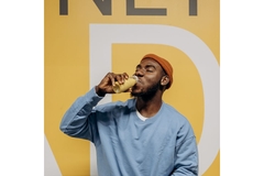 Man in blue sweater drinking from a bottle against yellow wall